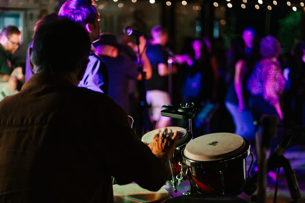 Hands playing congas at an Órale Band show with the crowd behind