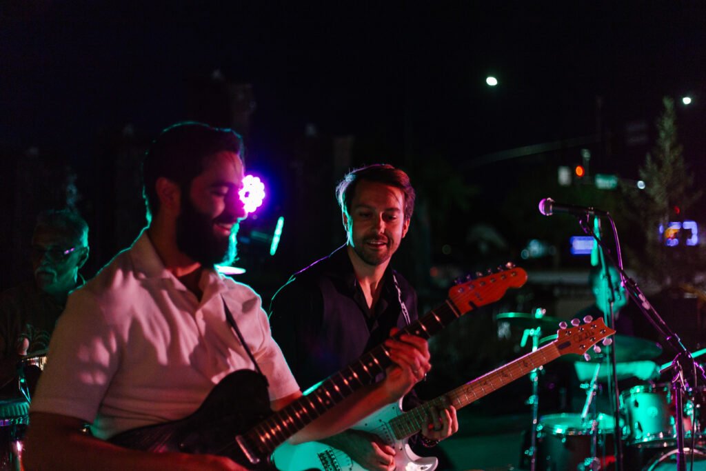 Two Órale Band guitarists playing side by side at an outdoor show