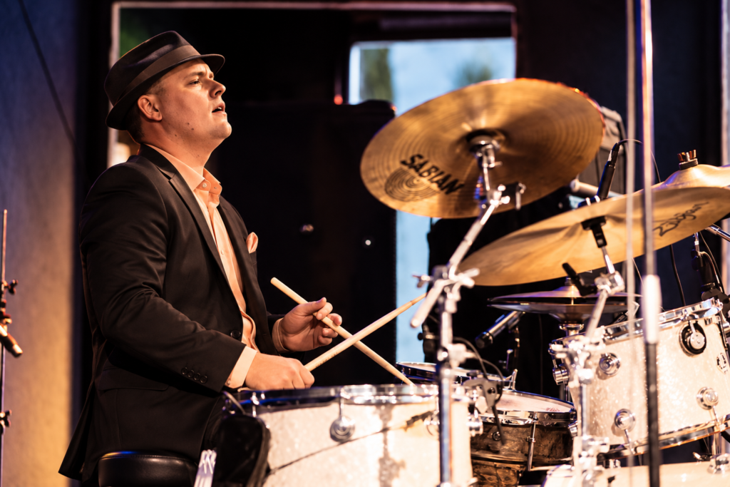 Órale Band drummer in a dark suit playing behind the kit