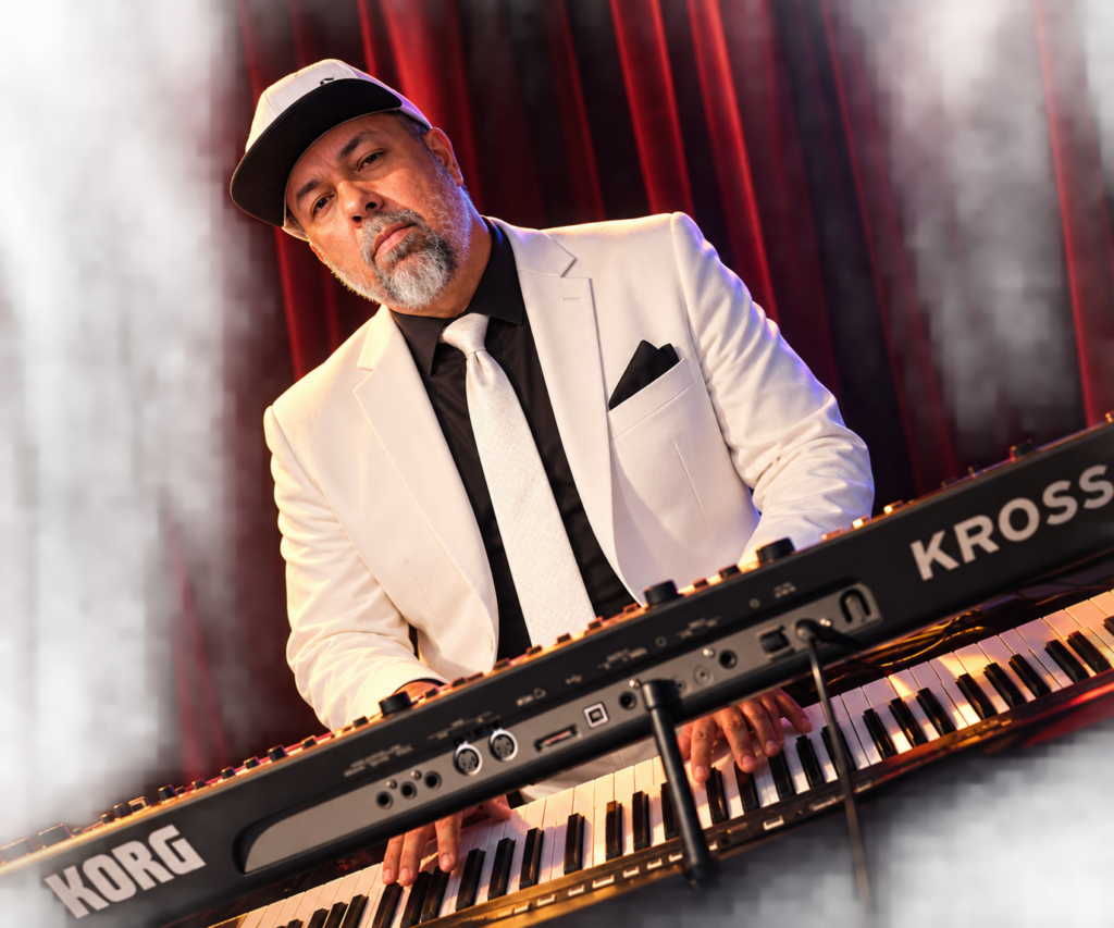 Órale Band keyboard player in a white suit at the keys during a live set